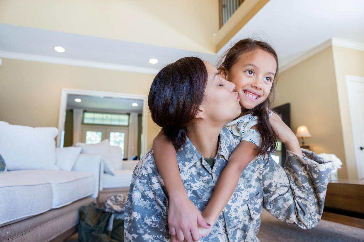 mother in uniform kisses smiling daughter on the cheek