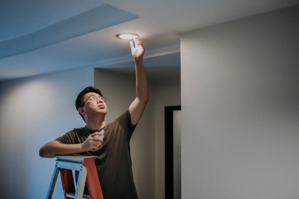 Man on ladder changes bulb in recessed ceiling fixture to an LED bulb. 