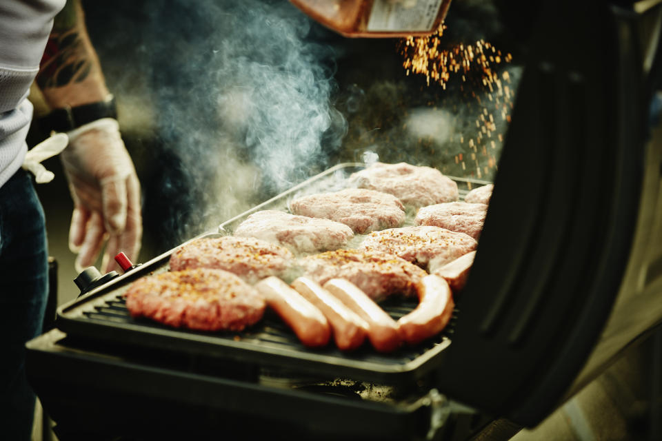 Man seasoning burgers and hot dogs on barbecue during tailgating party