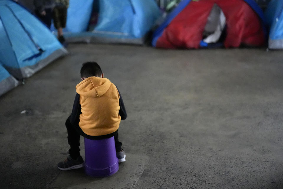 A boy, part of a family from the state of Mexico that has been awaiting for an asylum appointment through the CBP One app, sits on a bucket in a shelter for migrants, Saturday, Feb. 3, 2024, in Tijuana, Mexico. The family has been waiting for six months to receive an appointment to apply for asylum, living in a tent inside of the shelter. (AP Photo/Gregory Bull)