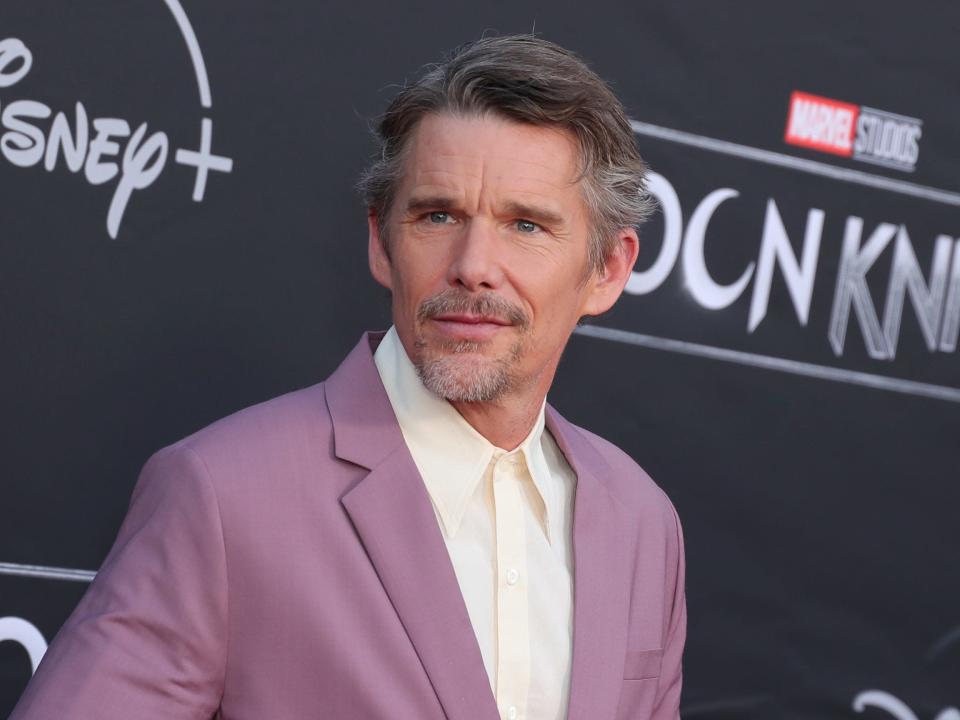 Ethan Hawke in a purple suit in front of a black background