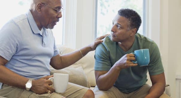 Senior father and son talking while having coffee on sofa