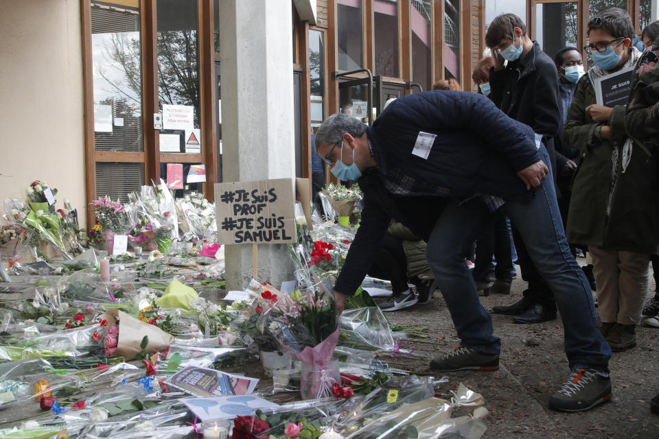 FILE - In this Oct. 17, 2020, file photo, a man lays a flower outside the school where a slain history teacher was working in Conflans-Sainte-Honorine, northwest of Paris. Scrubbing France clean of radicals and their breeding grounds is a priority cause of President Emmanuel Macron in a nation bloodied by terror attacks, including the beheading of a teacher outside his school followed by a deadly attack inside the basilica in Nice. (AP Photo/Michel Euler, File)