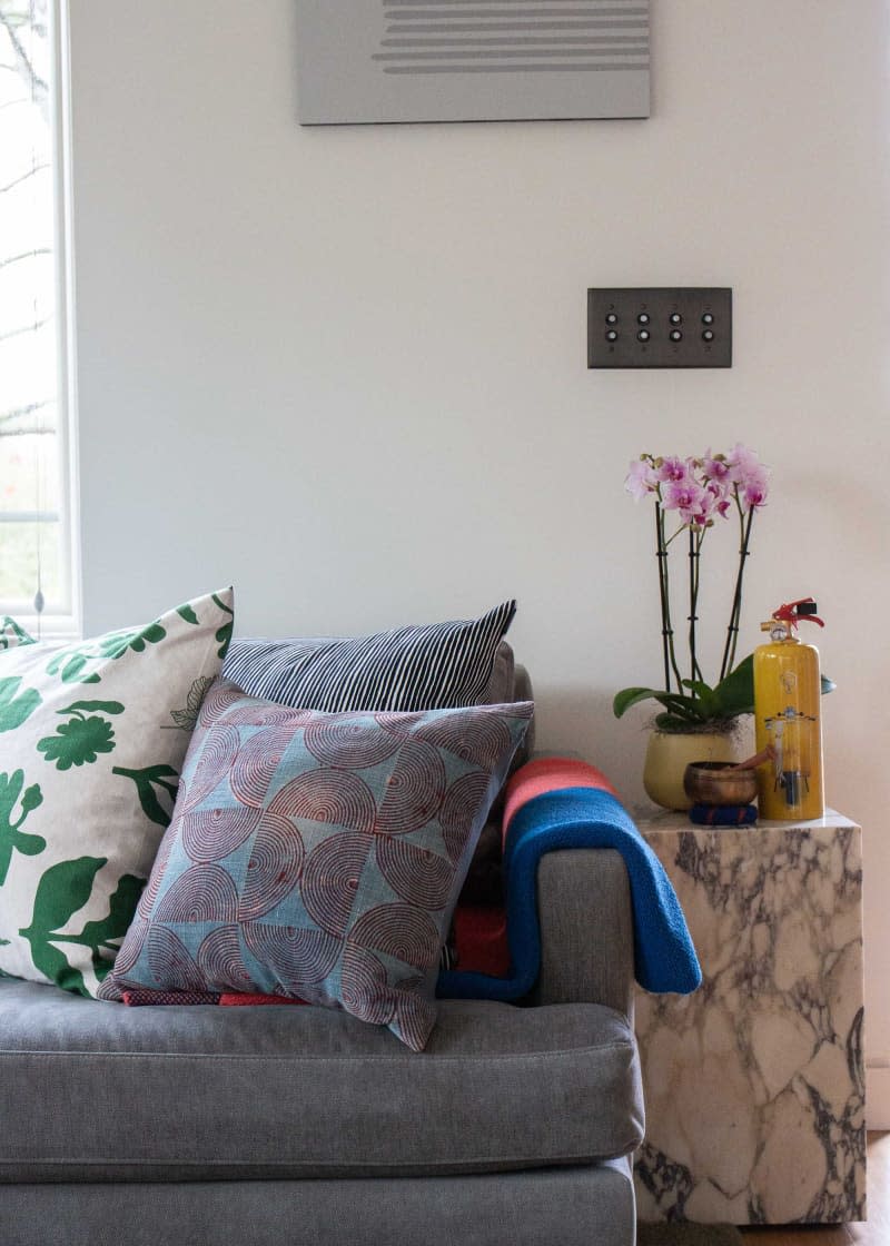 Marble side table beside sofa topped with decorative pillow and blanket.