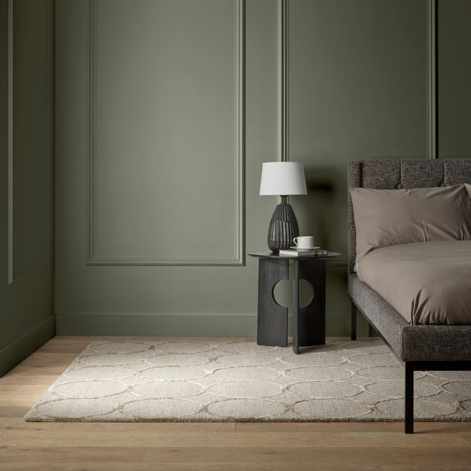 Green panelled wall with bed, bedside table, table lamp, and cream rug