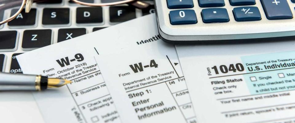 Close up of forms sitting on desk beside glasses, pen, calculator and keyboard.