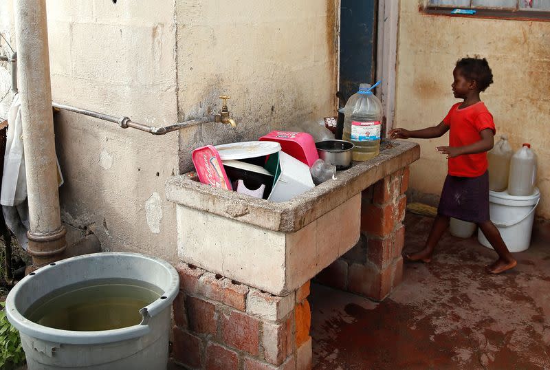 A child stands beside a pile of dishes sitting in a dry sink during a prolonged drought in Bulawayo