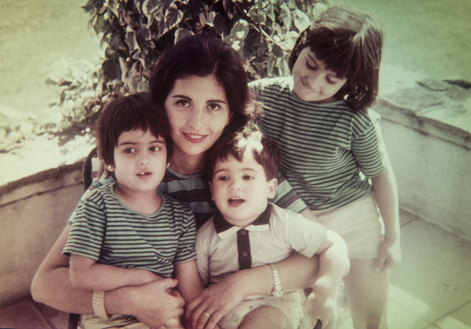 A vintage photo of a woman with two young children, one on each side, all smiling. They wear stripe-patterned outfits