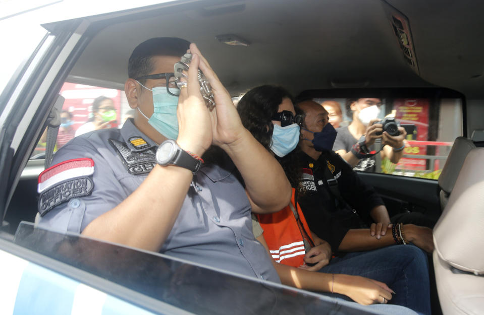 Indonesian immigration officers escorted Heather Mack of Chicago, Ill., center, sits in a car in Bali, Indonesia on Friday, Oct. 29, 2021. The American woman convicted of helping to kill her mother on Indonesia's tourist island of Bali in 2014 walked free from prison Friday after serving seven years of a 10-year sentence and will be deported to the United States.(AP Photo/Firdia Lisnawati)