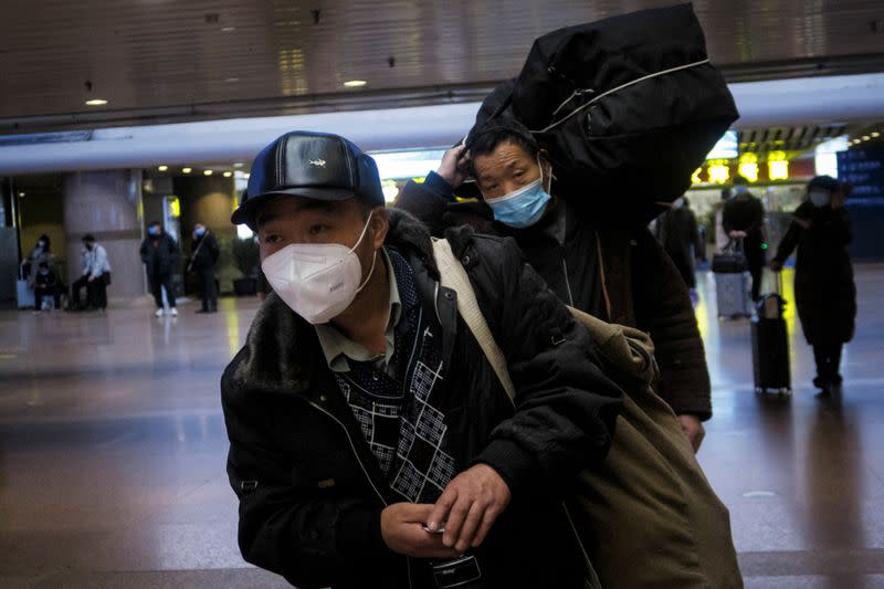 Travellers walk with their belongings at a railway station in Beijing