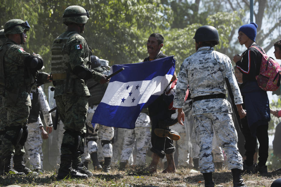 A Central American migrant holding a Honduran flag approaches Mexican security forces on the banks of the Suchiate River after a group of migrants crossed the river from Guatemala into Mexico near Ciudad Hidalgo, Mexico, Monday, Jan. 20, 2020. More than a thousand Central American migrants hoping to reach United States marooned in Guatemala are walking en masse across a river leading to Mexico in an attempt to convince authorities there to allow them passage through the country.(AP Photo/Marco Ugarte)