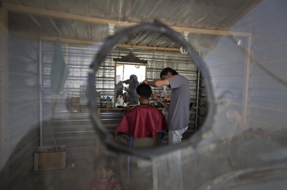 In this Thursday April 17, 2014 photo, a Syrian refugee gets a hair cut in a barbershop set up in a small metal shack at Zaatari refugee camp, near the Syrian border in Jordan. The shop operates in the heart of the now buzzing market that cuts through the camp and is the heart of Zaatari’s informal economy. (AP Photo/Khalil Hamra)