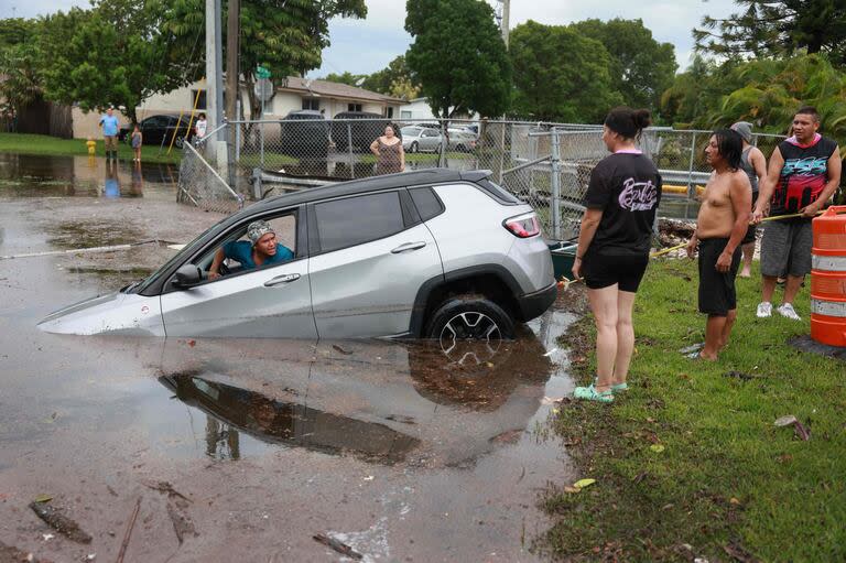 Un hombre  se sienta en un coche después de poner el vehículo en punto muerto mientras ayuda a intentar sacarlo del canal el 13 de junio de 2024, en Hallandale Beach, Florida.