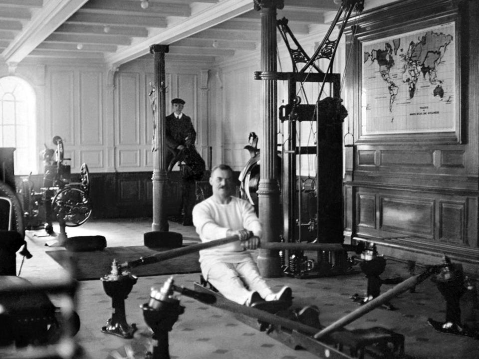 A black-and-white image of a group of people exercising in a large gymnasium on the Titanic.