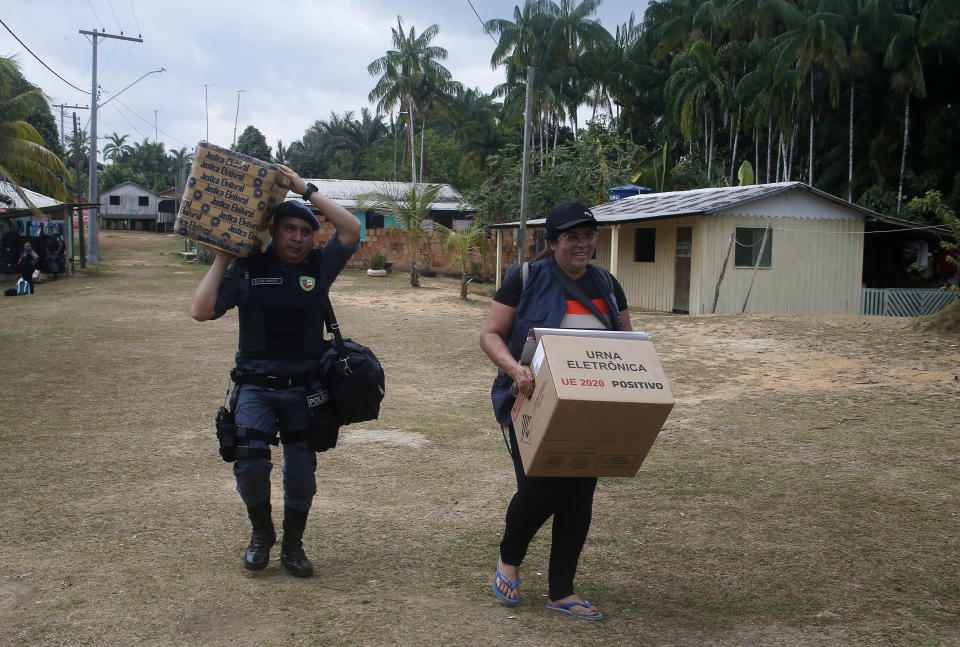 An electoral worker and a military police officer unload an electronic voting machine to be taken to a polling station a day ahead of the country's general elections, at the Bela Vista do Jaraqui community in Manaus, Amazonas state, Brazil, Saturday, Oct. 1, 2022. (AP Photo/Edmar Barros)