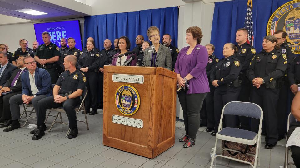 Flanked by officers from Jacksonville, its Beaches communities and Clay County, Hubbard House CEO Gail Patin (at podium) is joined by  Jennifer Rodriguez (left), CEO of St. Johns County's Quigley House, and Kelly Franklin (right), CEO of Clay County's Betty Griffin Center.