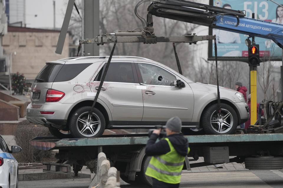 A cameraman films as a tow truck transports a car, which was damaged during clashes, from the central square in Almaty, Kazakhstan, Tuesday, Jan. 11, 2022. The president of Kazakhstan announced Tuesday that a Russia-led security alliance will start pulling out its troops from the country in two days after completing its mission. Life in Almaty, which was affected with the violence the most, started returning to normal this week, with public transport resuming operation and malls reopening. (AP Photo)