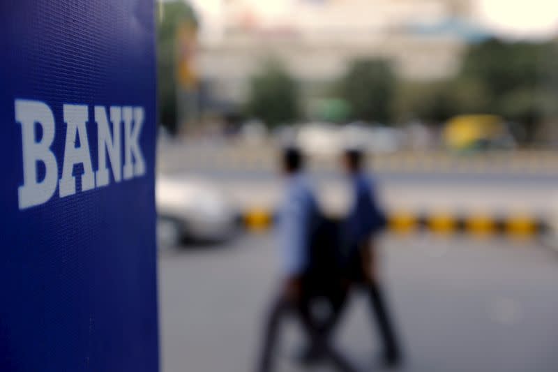 FILE PHOTO: Commuters walk past a bank sign along a road in New Delhi