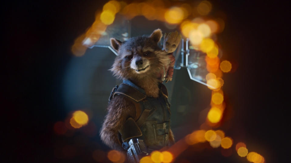 Rocket Raccoon with Baby Groot on his shoulder looks through the hole from a blaster and smiles in Guardians of the Galaxy Vol. 2