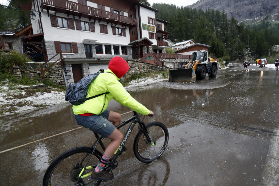 A supporter rides on a bicycle as a worker uses a digger to clean the road of the nineteenth stage of the Tour de France cycling race over 126,5 kilometers (78,60 miles) with start in Saint Jean De Maurienne and finish in Tignes, France, Friday, July 26, 2019. Tour de France organizers stopped Stage 19 of the race because of a hail storm as Julien Alaphilippe lost his yellow jersey to Egan Bernal. (AP Photo/Thibault Camus)