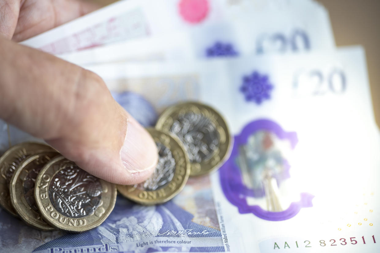 A man's hand holding £50 and £20 pound notes and pound coins