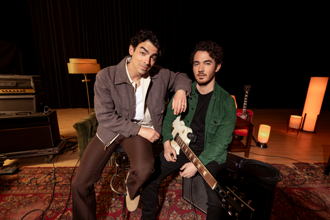 Joe and Kevin Jonas, seated and relaxed onstage