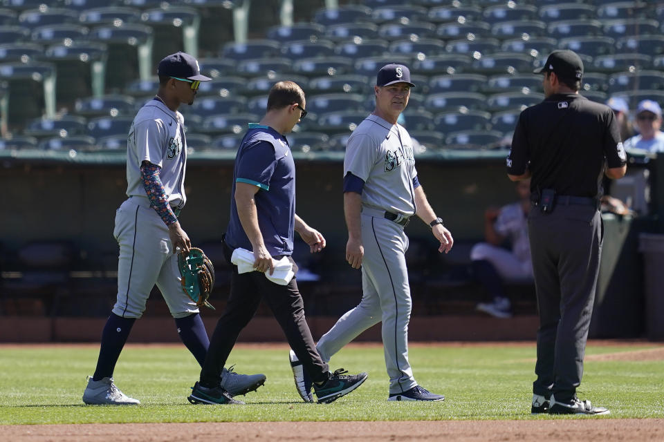 Seattle Mariners center fielder Julio Rodriguez, left, walks off the field with manager Scott Servais, middle right, and a trainer during the first inning of a baseball game against the Oakland Athletics in Oakland, Calif., Thursday, Sept. 22, 2022. (AP Photo/Jeff Chiu)