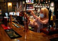 A woman wearing a face mask works behind a bar at the Grapes pub in Liverpool