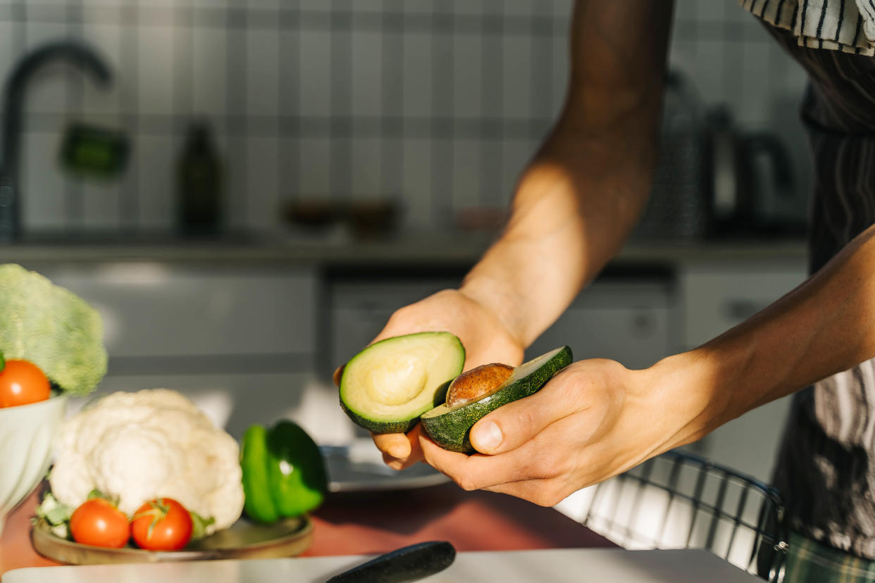 Young man cooking guacamole in light kitchen at home. Hands close-up.