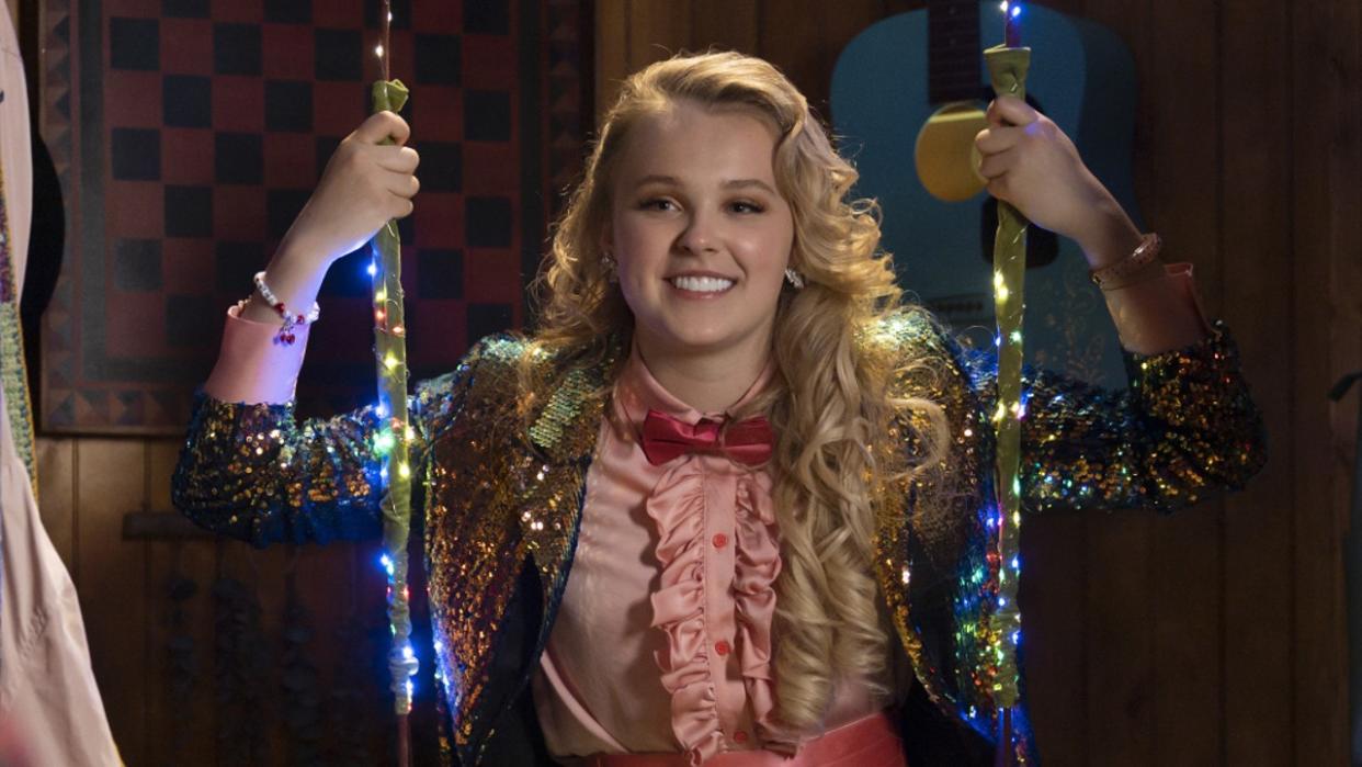  Jojo Siwa sitting on a light up swing in a sparkly suit on High School Musical: The Musical: The Series. 