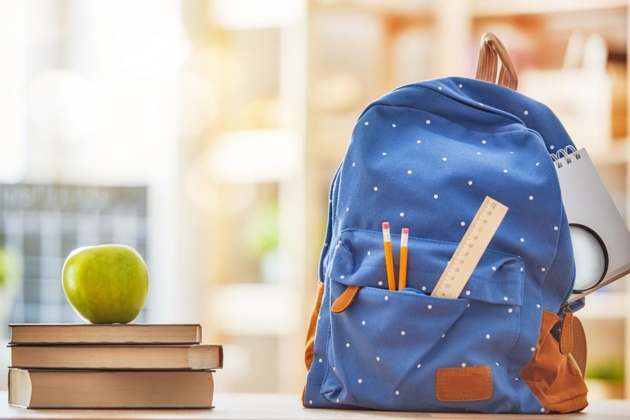 backpack with new school supplies sticking out, books with apple resting on them