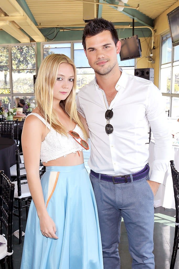 Billie Lourd in a crop top and skirt, and a man in a button-down shirt with sunglasses hanging from it, standing indoors