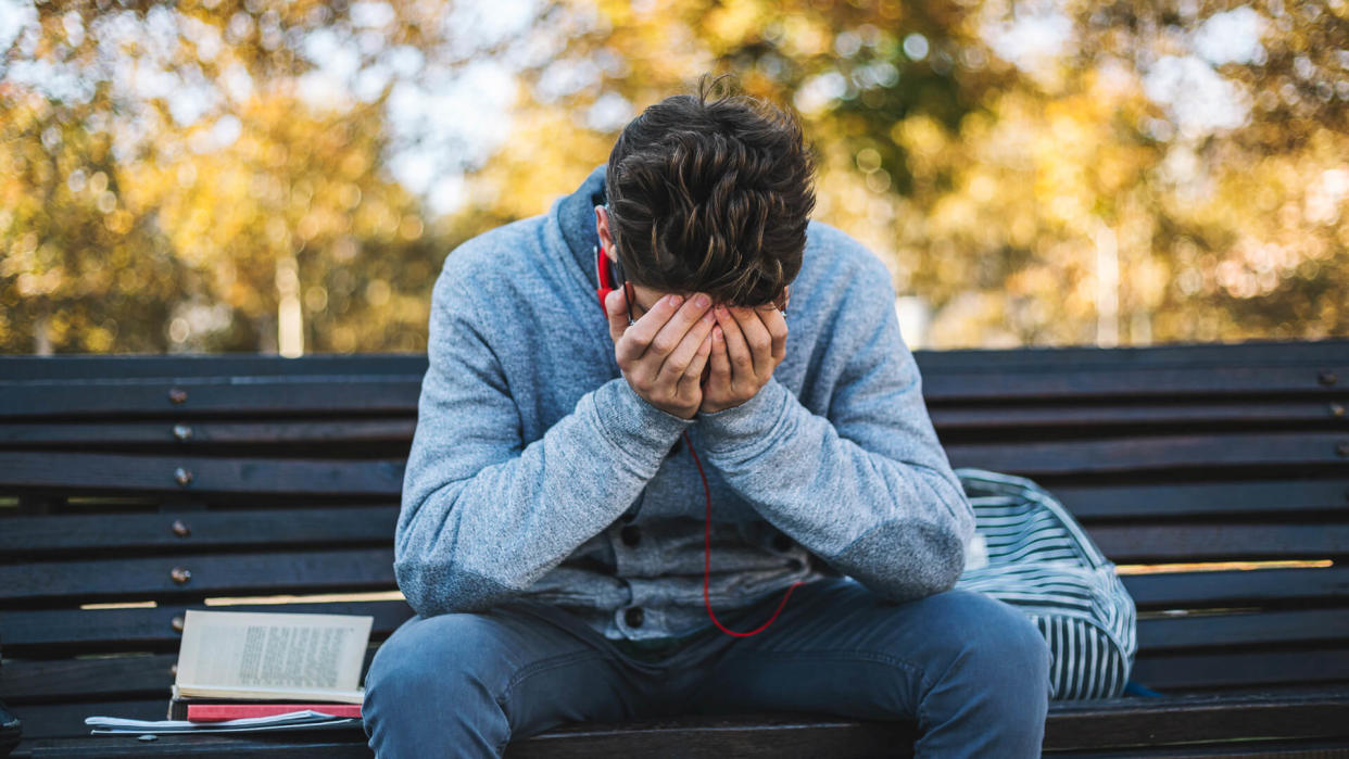 Teenager sits on a bench in the park and listen to music and learning for exame.