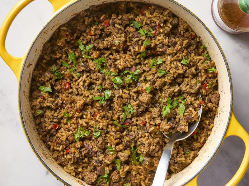 Overhead photo of a Dutch oven full of dirty rice garnished with cilantro with a bottle of hot sauce in the corner.