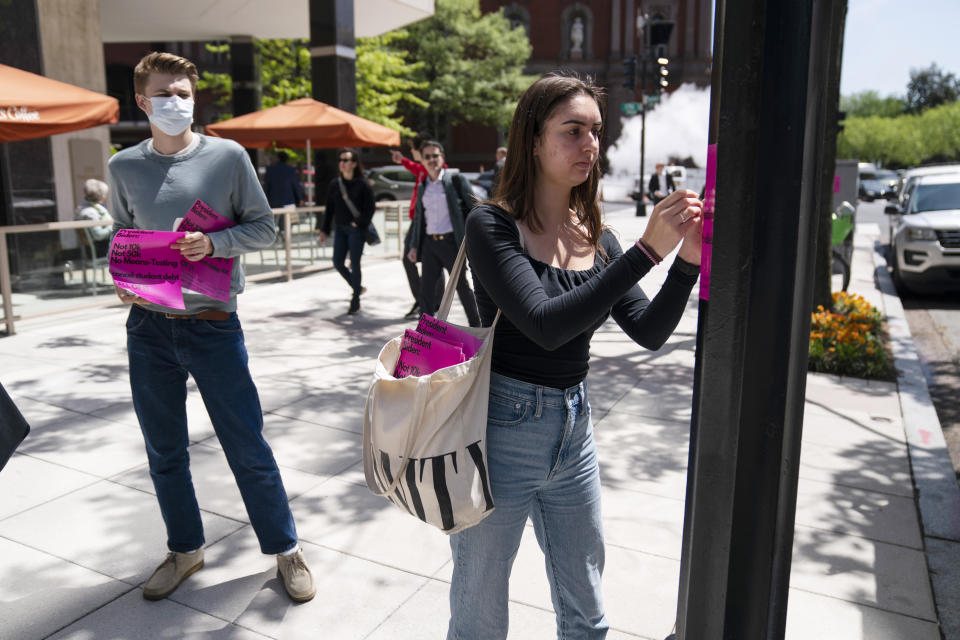 George Washington University student Kai Nilsen, left, watches as American University student Magnolia Mead as they put up posters near the White House promoting student loan debt forgiveness, Friday, April 29, 2022, in Washington. (AP Photo/Evan Vucci)