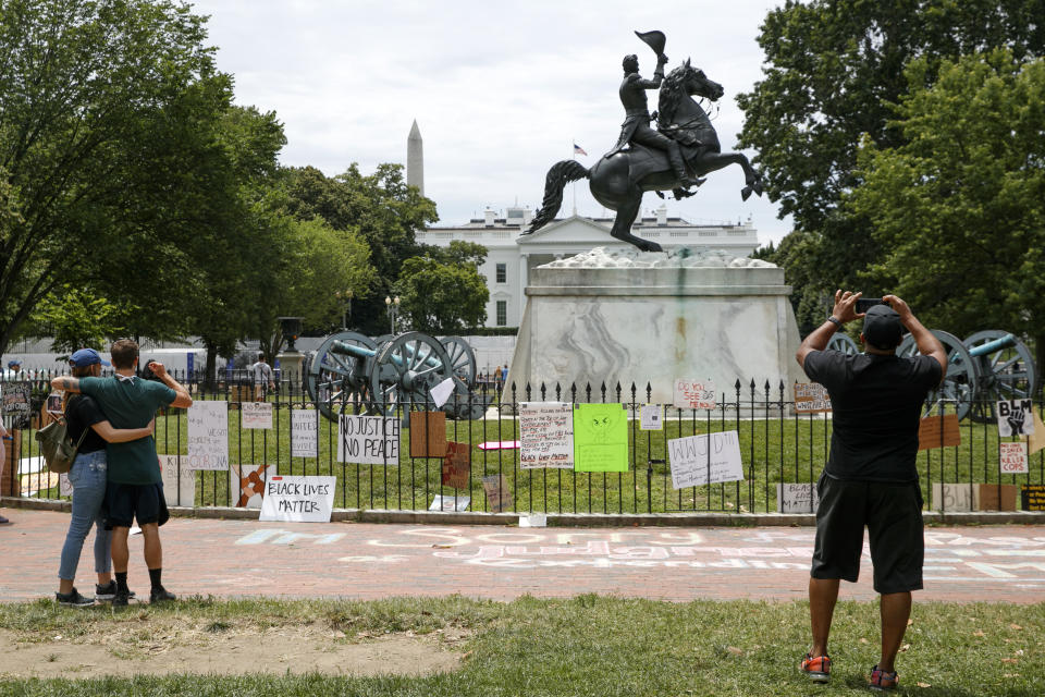 People visit Lafayette Park where protest signs are seen along the fencing that surrounds a statue of President Andrew Jackson, Tuesday, June 16, 2020, near the White House in Washington, where protests have occurred over the death of George Floyd, a black man who was in police custody in Minneapolis. (AP Photo/Jacquelyn Martin)