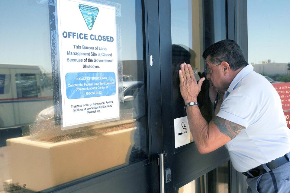 Letter carrier Jacob Ribald of the U.S. Postal Service peeks Oct. 1, 2013, into the window of the closed Bureau of Land Management office Las Cruces, N.M.  "I have a lot of mail for them,"  Ribald said. "At least I tried, right?" The Postal Service continued deliveries during the government shutdown while other federal agencies were shuttered.