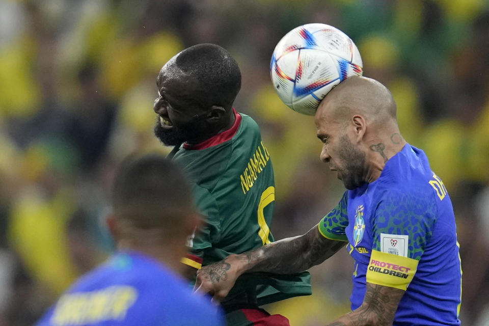 Brazil's Dani Alves, right, heads the ball past Cameroon's Moumi Ngamaleu during the World Cup group G soccer match between Cameroon and Brazil, at the Lusail Stadium in Lusail, Qatar, Friday, Dec. 2, 2022. (AP Photo/Natacha Pisarenko)