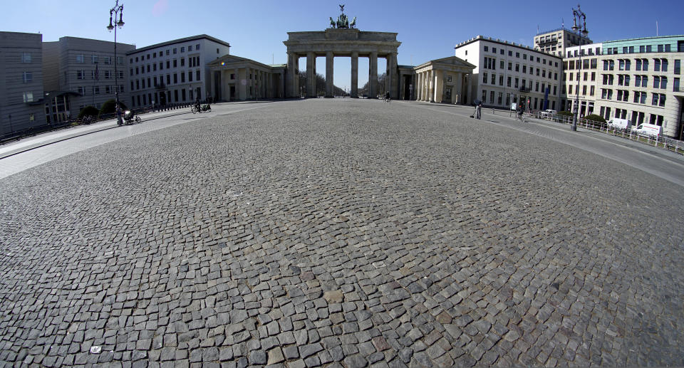 Only a few people visit the square in front of the Brandenburg Gate in Berlin, Germany, Tuesday, March 24, 2020. In order to slow down the spread of the coronavirus, the German government has considerably restricted public life and asked the citizens to stay at home and keep distance from other people. (AP Photo/Michael Sohn)