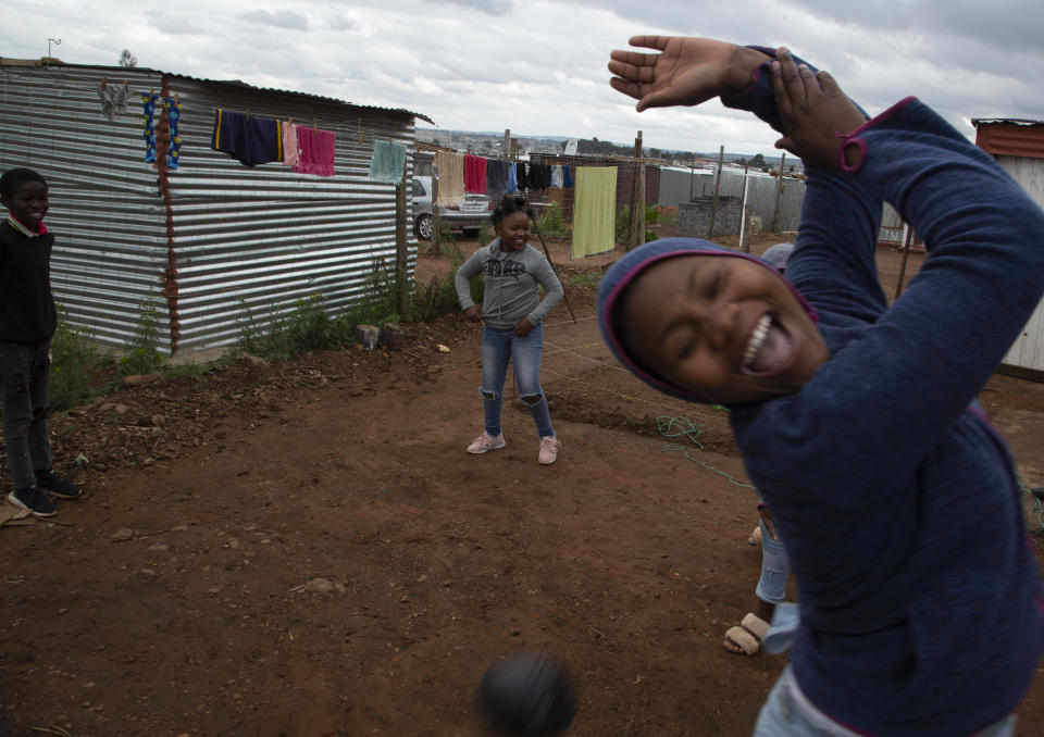 Lilitha Jiphethu, 11, background center, plays with her friends with a ball made from discarded plastic grocery bags, outside her home in Orange Farm, South Africa, on Tuesday, April 28, 2020. Like many children under lockdown, she misses her friends and her teachers, but understands why school is closed and why they are being kept at home. (AP Photo/Denis Farrell)