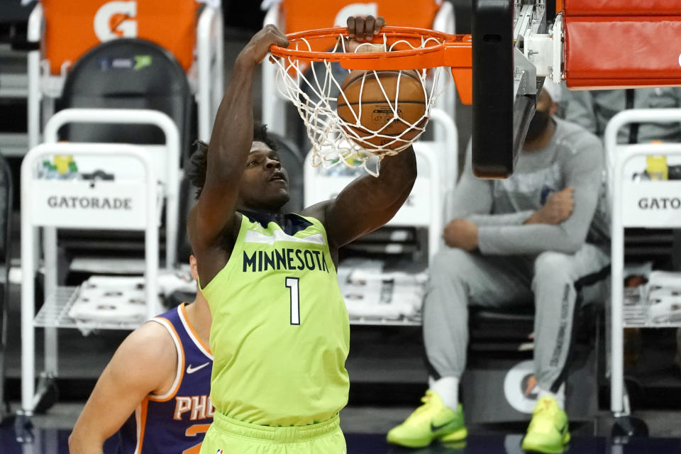 Anthony Edwards with two hands on the rim after a dunk.