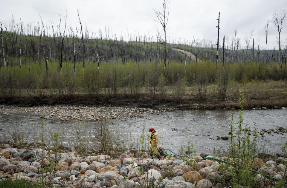 A firefighter monitors a pump in a river bed used for wildfire sprinklers in the evacuated neighborhood of Grayling Terrace in Fort McMurray, Alta., Thursday, May 16, 2024. (Jeff McIntosh/The Canadian Press via AP)