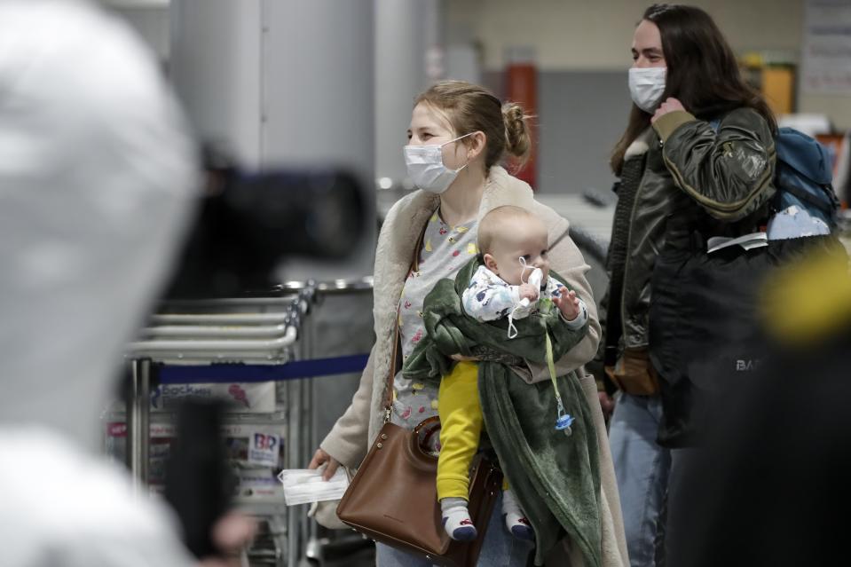 A passengers wearing face mask with her baby walks to medical experts to be checked after arriving from a foreign country at Sheremetyevo airport outside Moscow, Russia, Thursday, March 19, 2020. Authorities in Russia are taking vast measures to prevent the spread of the disease in the country. The measures include closing the border for all foreigners, shutting down schools for three weeks, sweeping testing and urging people to stay home. For most people, the new coronavirus causes only mild or moderate symptoms. For some it can cause more severe illness. (AP Photo/Pavel Golovkin)