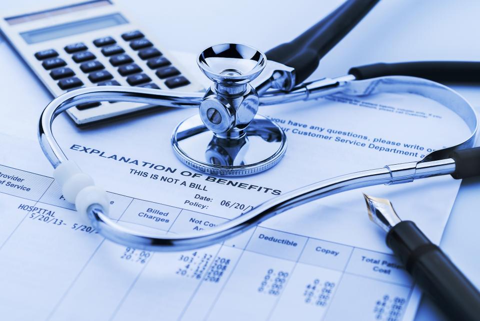 Stethoscope and pen and calculator on top of an explanation of health insurance benefits.