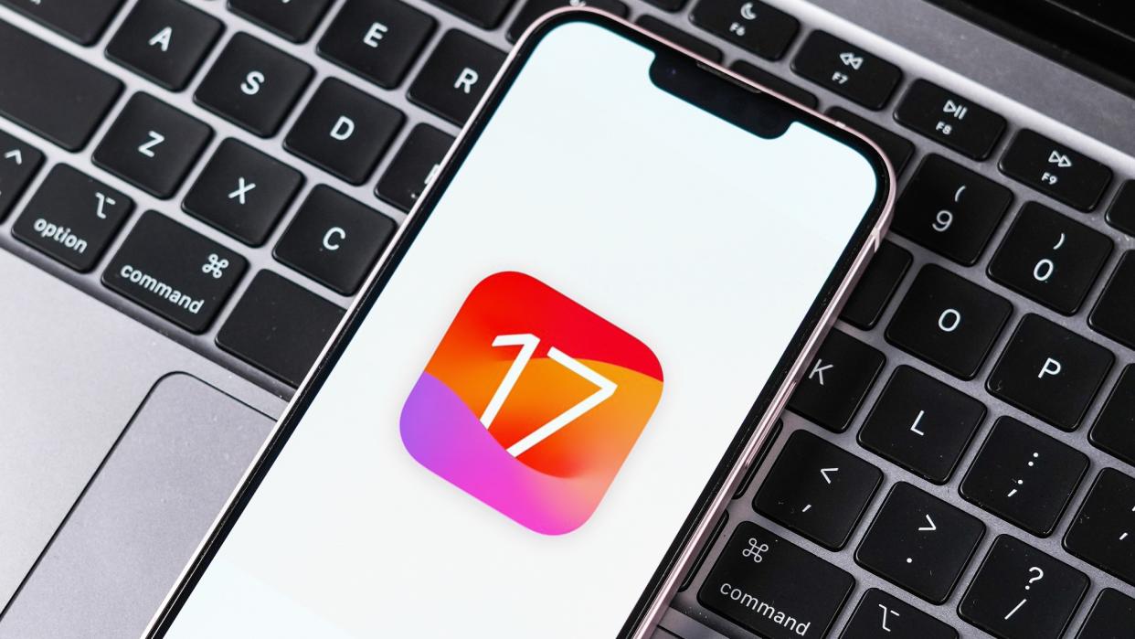  IOS 17 logo on iPhone sitting on MacBook keyboard . 