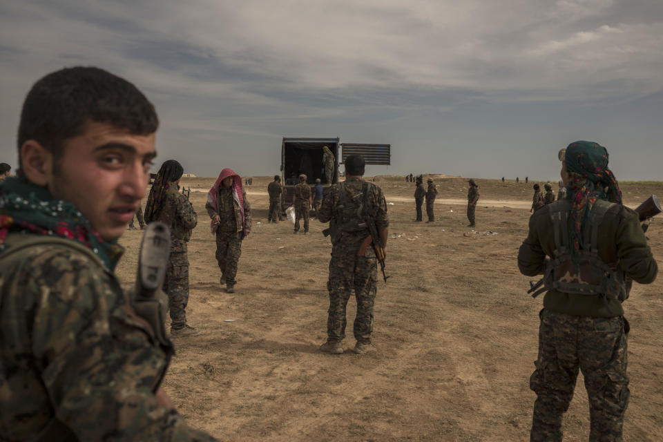 In this Sunday, March 10, 2019 photo, U.S.-backed Syrian forces stand guard as civilians wounded by airstrikes, during an offensive on the last area held by Islamic State group extremists, arrive by truck at a reception area for evacuees, in Syria's eastern Deir el-Zour province near the Iraqi border, outside of Baghouz, Syria.