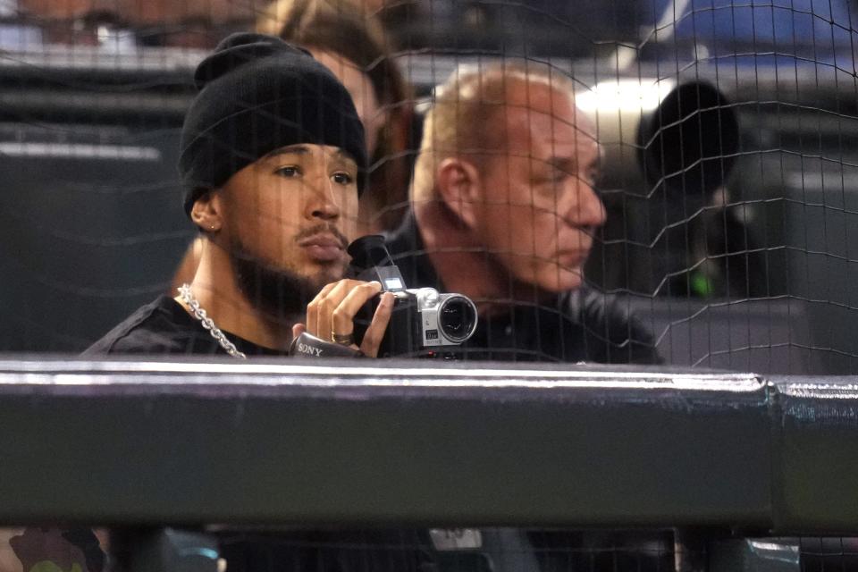 Phoenix Suns guard Devin Booker (center), with old school camcorder in tow, watches the game between the Arizona Diamondbacks and the Philadelphia Phillies during the fourth inning in Game 4 of the NLCS of the 2023 MLB playoffs at Chase Field in Phoenix on Oct. 20, 2023.