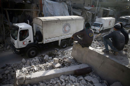 Civil defence members sit amid the rubble as they watch an aid convoy of Syrian Arab Red Crescent driving through the besieged town of Douma, Eastern Ghouta, Damascus, Syria March 5, 2018. REUTERS/Bassam Khabieh