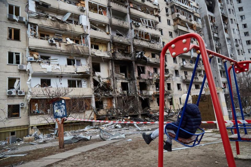 A child sits on a swing across from a residential building destroyed by a Russian attack in Kyiv, Ukraine, on Feb. 25, 2022. (Pierre Crom/Getty Images)