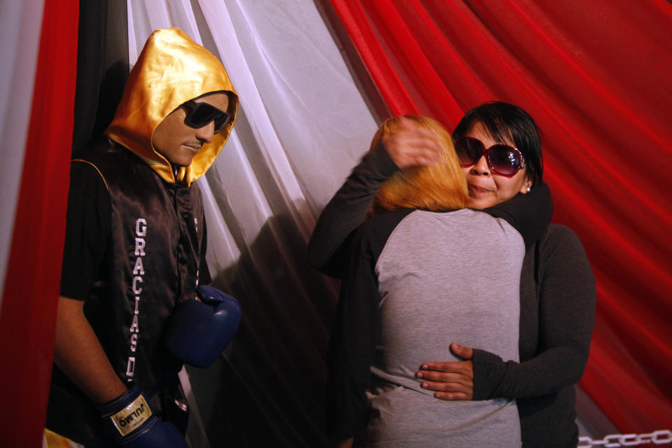 Lidianette Carmona, right, the wife of the late boxer Christopher Rivera who was shot to death on Sunday, left, hugs the boxer's mother Celines Amaro, as they stand next to his body propped up in a fake boxing ring during his wake at the community recreation center within the public housing project where he lived in San Juan, Puerto Rico, Friday, Jan. 31, 2014. Elsie Rodriguez, vice president of the Marin funeral home, explained that Rivera had asked his family that if he died, he wanted his funeral to make reference to his boxing career. (AP Photo/Ricardo Arduengo)